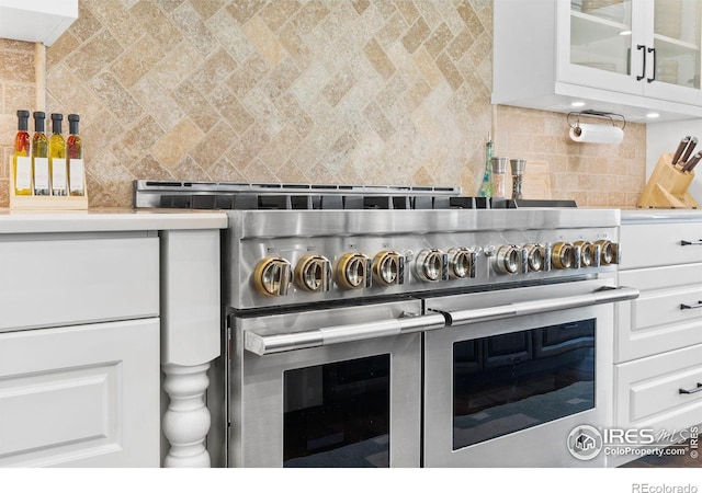 room details featuring backsplash, white cabinetry, and range with two ovens