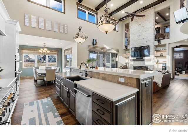 kitchen featuring a kitchen island with sink, sink, stainless steel dishwasher, beamed ceiling, and dark brown cabinets