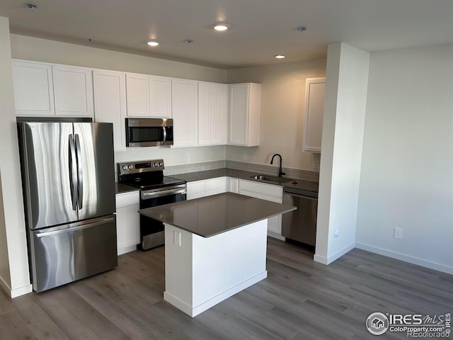 kitchen with white cabinetry, sink, stainless steel appliances, a kitchen island, and hardwood / wood-style flooring