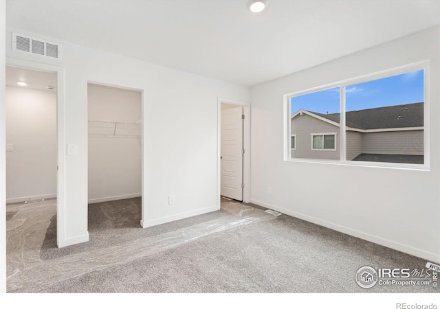 unfurnished bedroom with a walk in closet, a closet, and light carpet