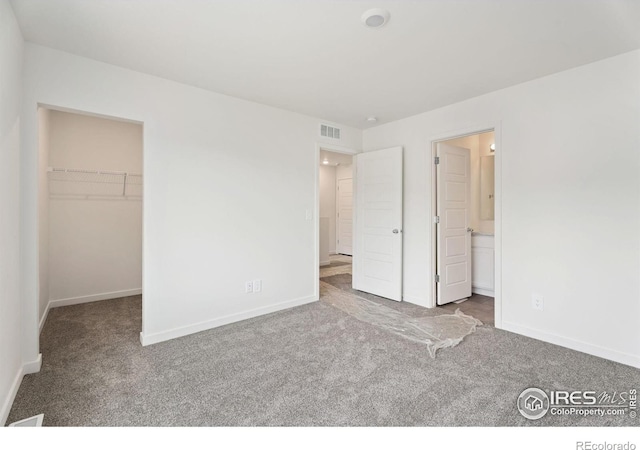 unfurnished bedroom featuring a closet, a spacious closet, ensuite bathroom, and carpet flooring