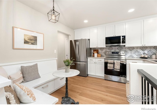 kitchen with decorative light fixtures, light wood-type flooring, backsplash, white cabinets, and appliances with stainless steel finishes