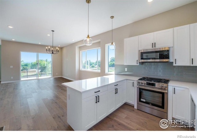 kitchen with white cabinetry, appliances with stainless steel finishes, kitchen peninsula, and hanging light fixtures