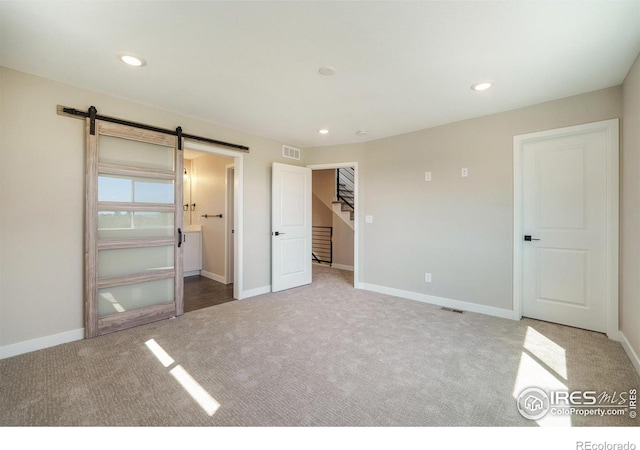 unfurnished bedroom featuring connected bathroom, carpet flooring, and a barn door