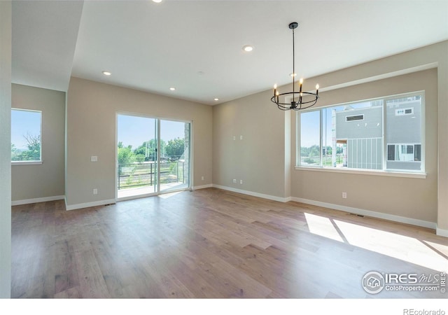 unfurnished room featuring plenty of natural light, a chandelier, and light hardwood / wood-style flooring