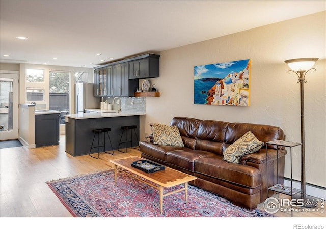 living room featuring light hardwood / wood-style floors, baseboard heating, and sink