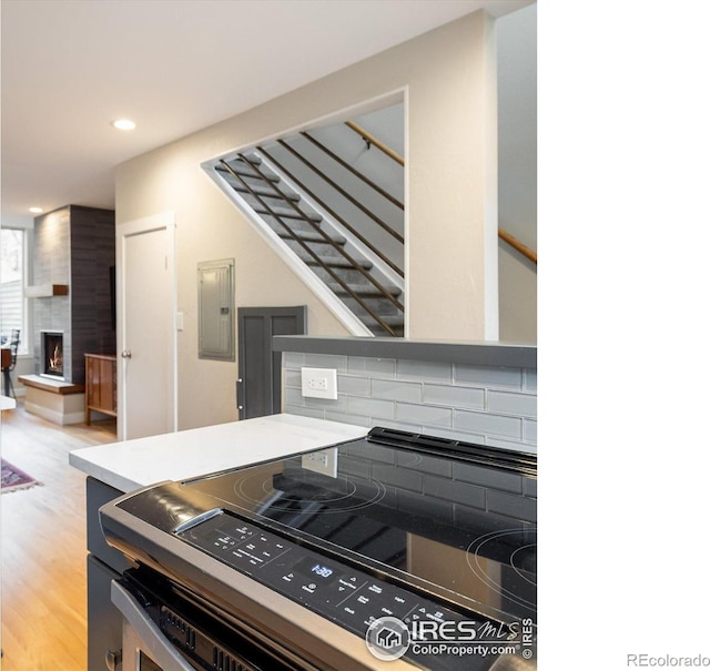 kitchen with electric panel, hardwood / wood-style floors, decorative backsplash, a fireplace, and range