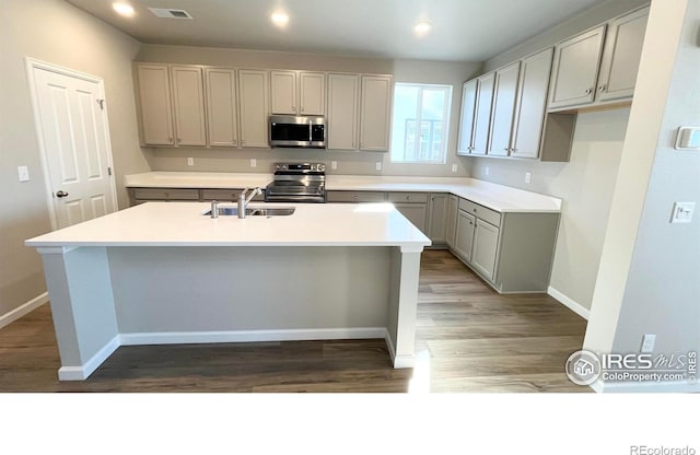 kitchen featuring stainless steel appliances, a sink, visible vents, gray cabinets, and a center island with sink