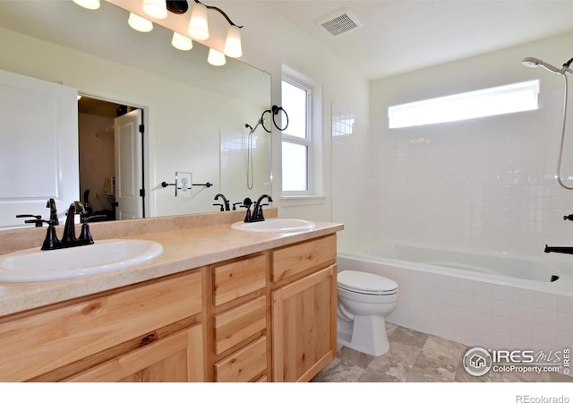 bathroom with visible vents, toilet, double vanity, tiled shower / bath, and a sink