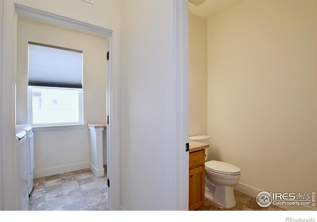 bathroom featuring washing machine and clothes dryer, toilet, vanity, and baseboards