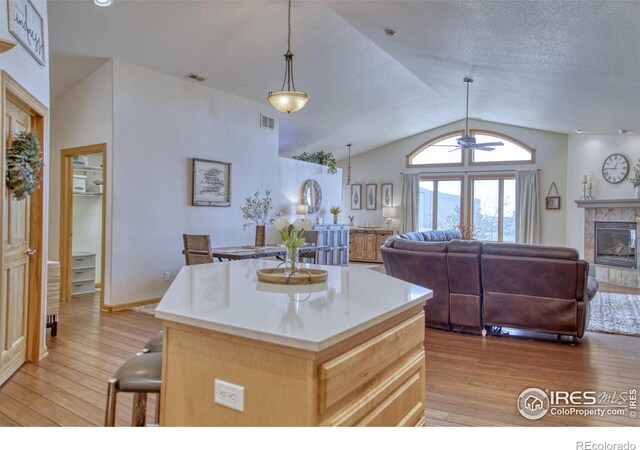 kitchen featuring light brown cabinetry, vaulted ceiling, light hardwood / wood-style flooring, a fireplace, and a center island