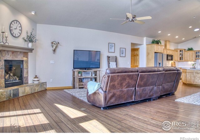 living room featuring ceiling fan, lofted ceiling, a tile fireplace, and light hardwood / wood-style flooring