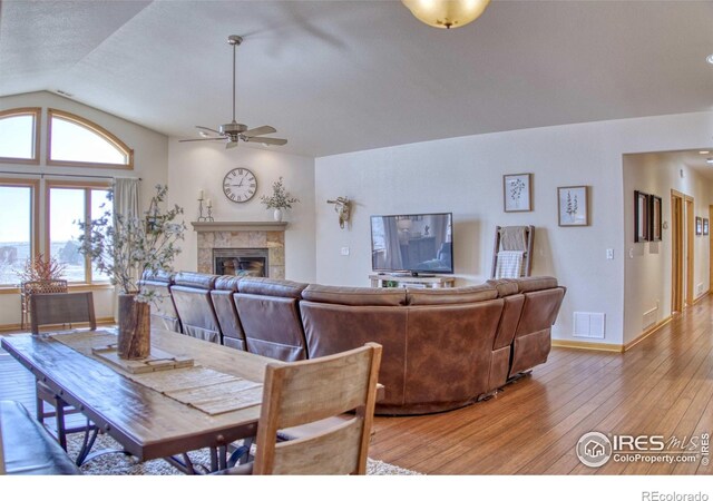 dining room featuring ceiling fan, hardwood / wood-style floors, a textured ceiling, vaulted ceiling, and a fireplace