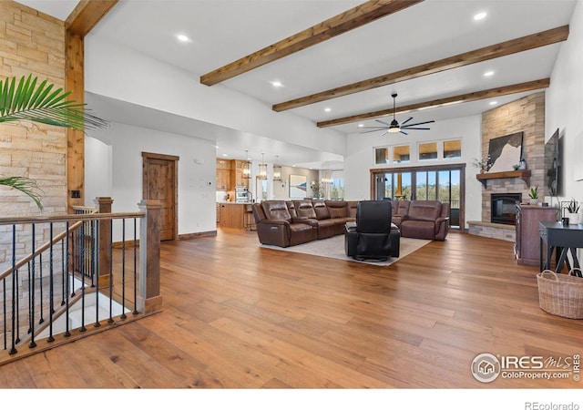 living room featuring beamed ceiling, ceiling fan, a stone fireplace, and light wood-type flooring