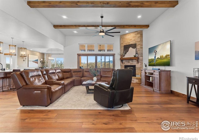 living room with beam ceiling, light hardwood / wood-style flooring, a stone fireplace, and ceiling fan