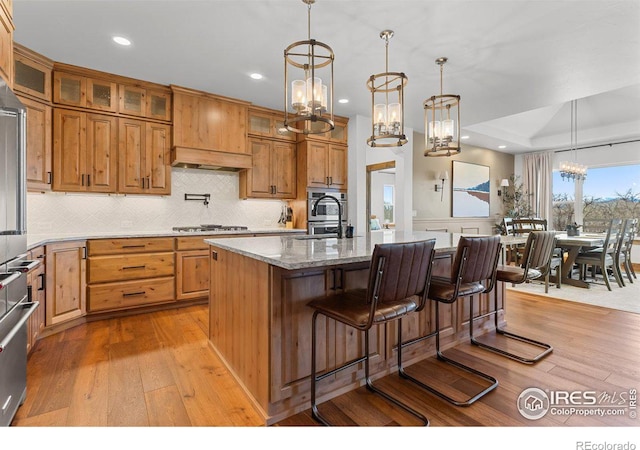 kitchen with light stone countertops, a kitchen breakfast bar, a kitchen island with sink, decorative light fixtures, and light hardwood / wood-style flooring