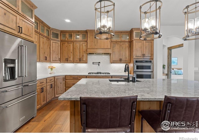 kitchen featuring pendant lighting, backsplash, sink, light stone counters, and stainless steel appliances