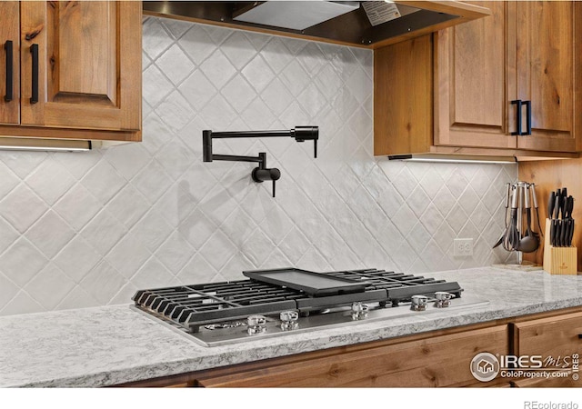 kitchen with wall chimney exhaust hood, decorative backsplash, light stone counters, and stainless steel gas cooktop