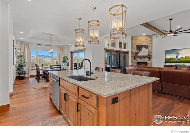 kitchen featuring light stone countertops, sink, a center island with sink, a fireplace, and hanging light fixtures