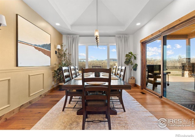 dining room with hardwood / wood-style flooring, a notable chandelier, a raised ceiling, and vaulted ceiling