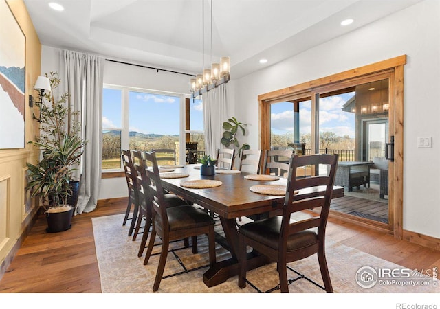 dining area with a raised ceiling, a mountain view, a notable chandelier, and light wood-type flooring