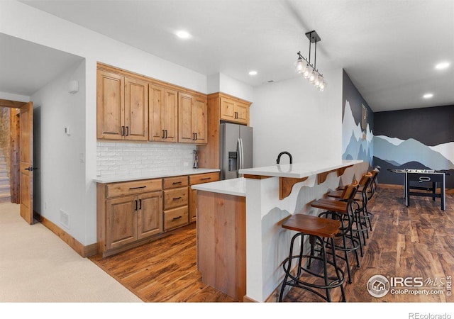 kitchen with tasteful backsplash, dark hardwood / wood-style floors, stainless steel fridge, pendant lighting, and a kitchen island with sink