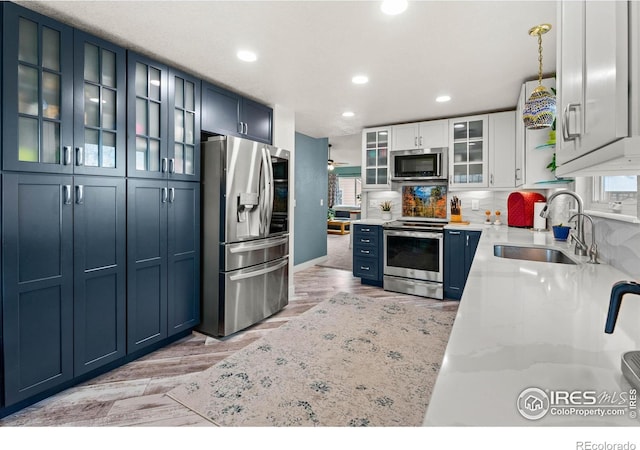 kitchen featuring white cabinets, sink, hanging light fixtures, light stone countertops, and stainless steel appliances