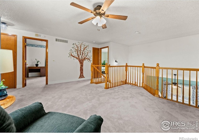 sitting room with a textured ceiling, ceiling fan, and light carpet