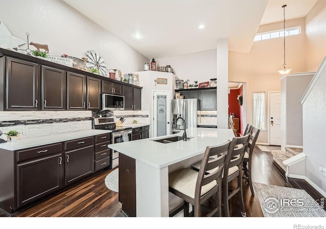 kitchen featuring appliances with stainless steel finishes, a kitchen breakfast bar, sink, a center island with sink, and hanging light fixtures