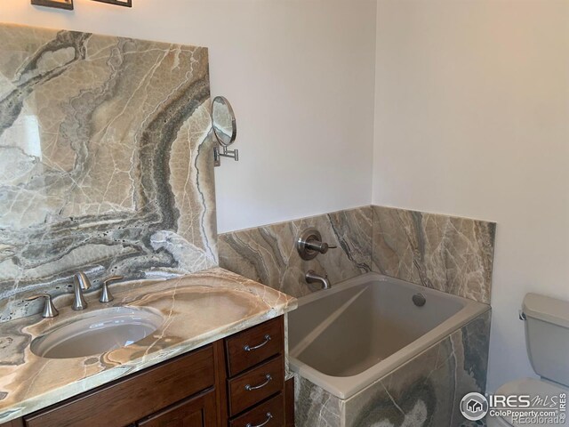 bathroom featuring vanity, tiled bath, and toilet