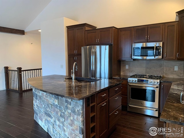 kitchen featuring lofted ceiling, sink, appliances with stainless steel finishes, a kitchen island with sink, and dark stone counters