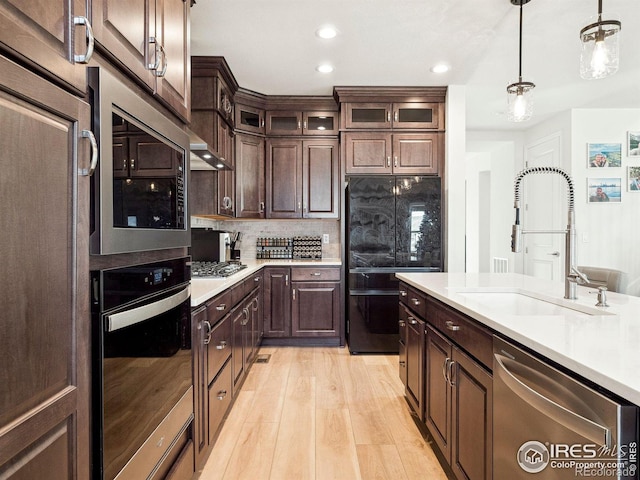 kitchen featuring sink, light wood-type flooring, decorative light fixtures, dark brown cabinetry, and stainless steel appliances