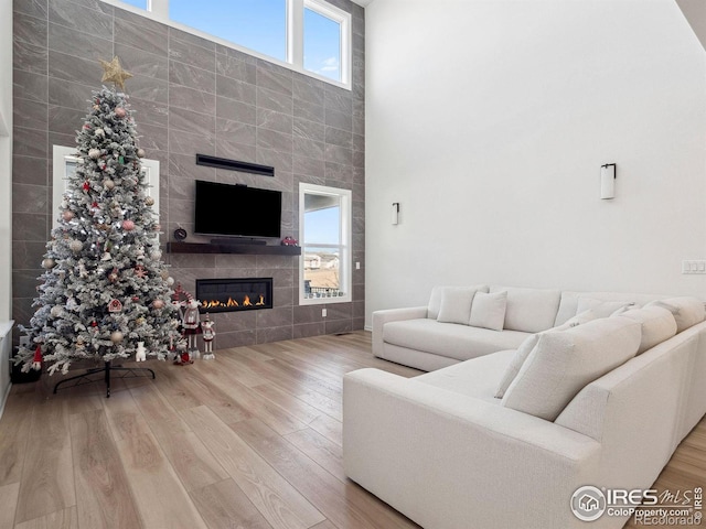 living room featuring wood-type flooring, a high ceiling, and a tiled fireplace