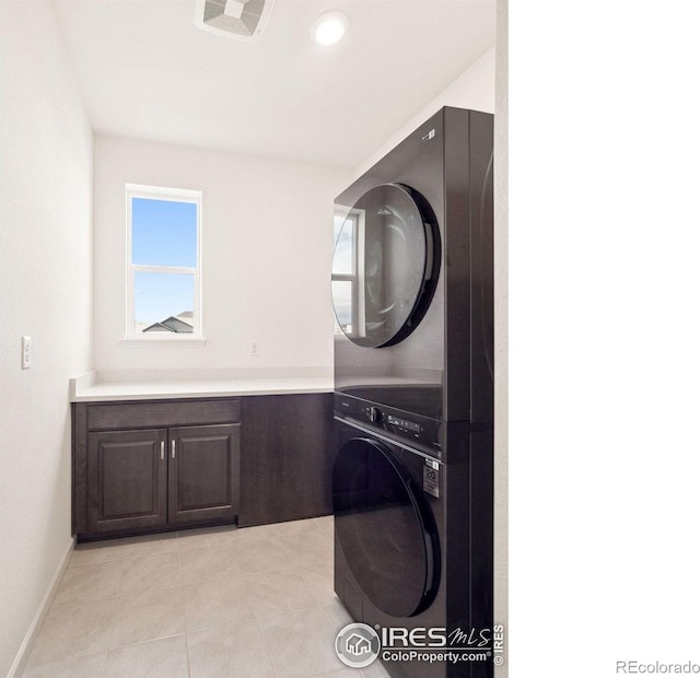 laundry room featuring cabinets, stacked washer and clothes dryer, and light tile patterned flooring