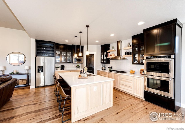 kitchen with pendant lighting, an island with sink, decorative backsplash, exhaust hood, and stainless steel appliances