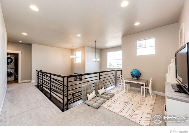 corridor with light carpet, stacked washer and clothes dryer, and a chandelier