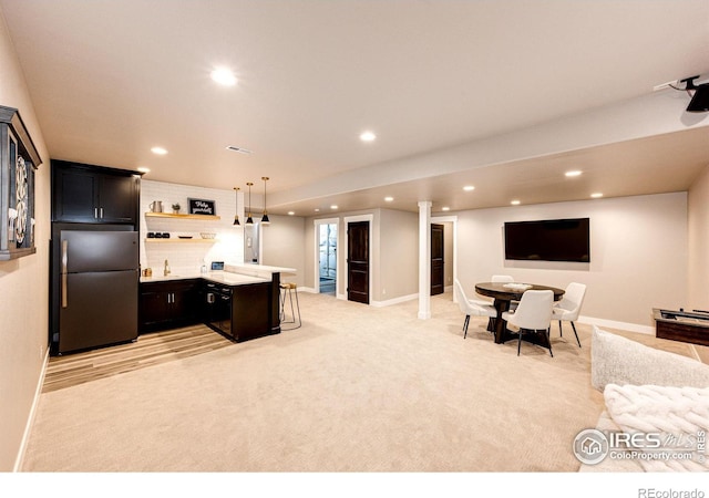 kitchen with stainless steel refrigerator, light colored carpet, a kitchen bar, and hanging light fixtures