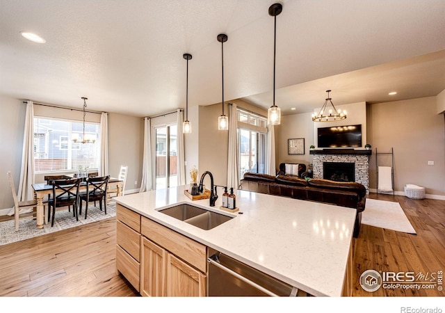 kitchen with sink, stainless steel dishwasher, an island with sink, a notable chandelier, and a fireplace