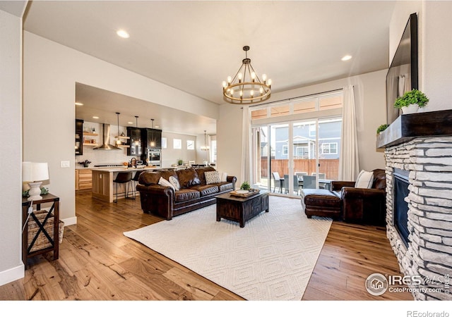 living room featuring hardwood / wood-style floors, a stone fireplace, and a notable chandelier