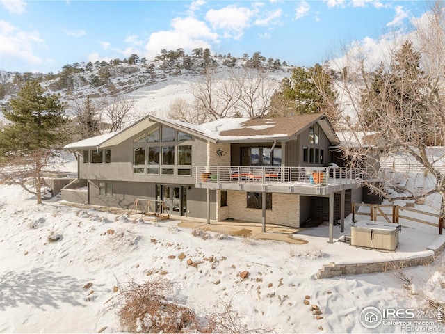 snow covered back of property with a wooden deck and a hot tub