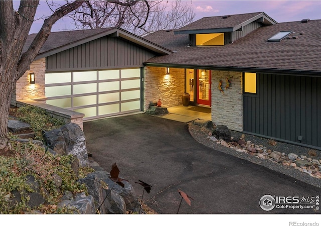 view of front facade with stone siding, a garage, driveway, and a shingled roof