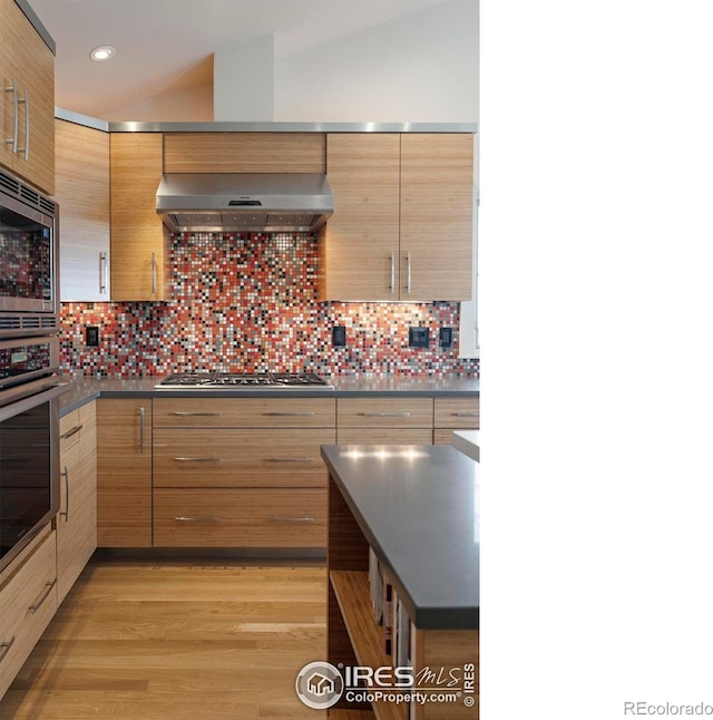 kitchen featuring ventilation hood, lofted ceiling, appliances with stainless steel finishes, dark countertops, and backsplash