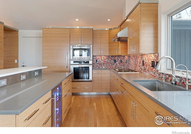 kitchen featuring a sink, wine cooler, under cabinet range hood, appliances with stainless steel finishes, and backsplash