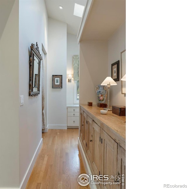 hallway with a skylight, baseboards, and light wood-type flooring