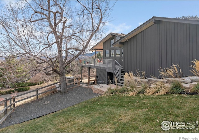 view of side of home featuring fence, stairs, a lawn, a deck, and a patio