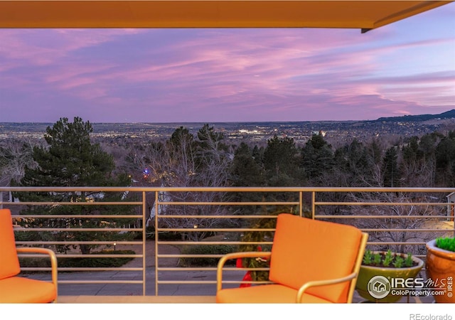 balcony at dusk featuring a view of trees