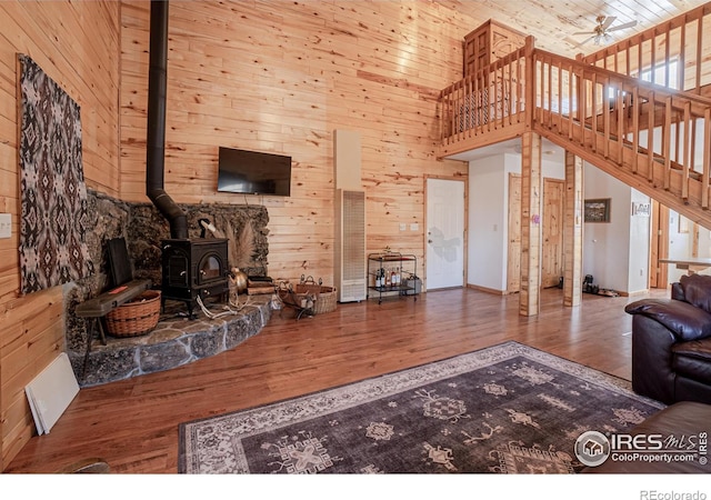 living room featuring ceiling fan, hardwood / wood-style floors, a high ceiling, a wood stove, and wood walls