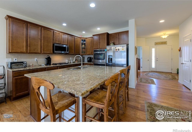 kitchen featuring light stone countertops, stainless steel appliances, a kitchen island with sink, sink, and light hardwood / wood-style floors