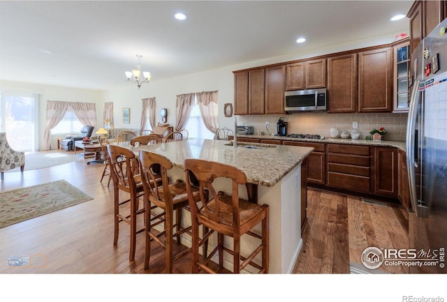 kitchen featuring light stone counters, stainless steel appliances, a kitchen island with sink, and dark wood-type flooring