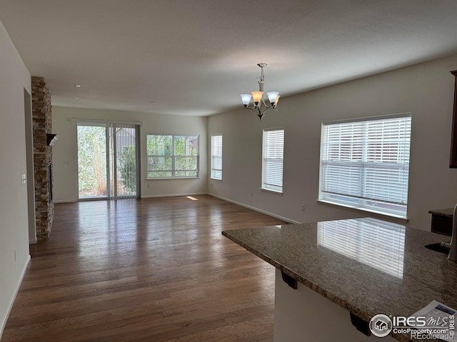 unfurnished living room featuring dark wood-style flooring, a notable chandelier, and baseboards